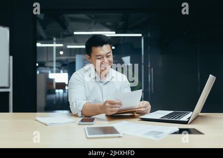 Happy and successful asian businessman reading financial document letter, boss working with documents in office, paperwork Stock Photo