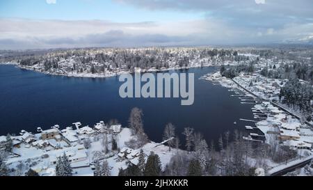 An aerial drone view of Lake Stevens surrounded by trees and houses covered in snow Stock Photo