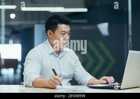 Serious and focused asian male accountant working with documents in modern office, businessman behind paper work Stock Photo