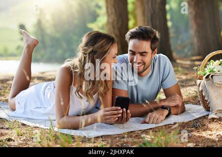 The selfie we just took is my new favourite picture. a couple looking at something on a digital tablet while having a picnic in the forest. Stock Photo