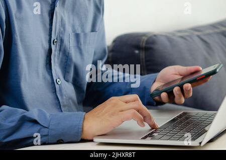 Businessman hand typing keyboard on laptop computer with smart phone. Close up businessman communicating internet and social media at his desk. Stock Photo
