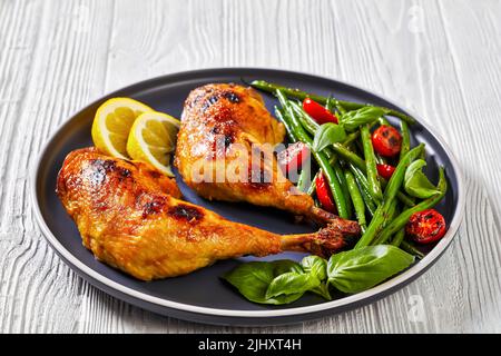 roast chicken legs with green beans, lemon, fried tomatoes and fresh basil on plate on white  textured wooden table Stock Photo