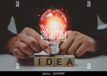 Text idea with a hand holding a light bulb Innovative wood cube block solution. Stock Photo