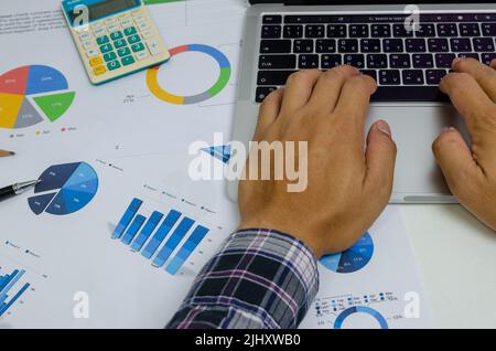 Businessman person hand using keyboard computer laptop with document chart finance and graph report investment at office.Paperwork management analysis Stock Photo