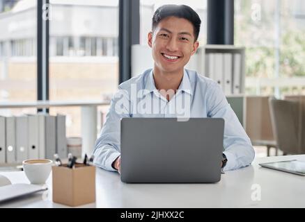 Asian businessman working on his laptop. Portrait of young asian businessman working in a modern office. Happy businessman typing on his laptop Stock Photo
