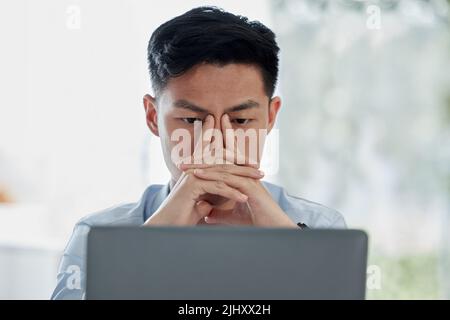 Stressed asian businessman using an office laptop. Thinking professional sitting alone and browsing the internet on technology. Anxious man searching Stock Photo