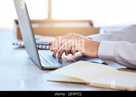 Closeup of male hands typing on laptop keyboard. Businessman using laptop to type email or do online research while sitting at desk Stock Photo