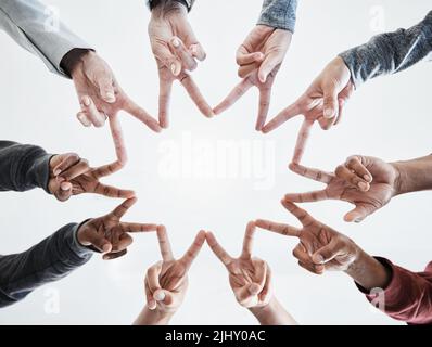 Below hands in circle making a star shape. A group of people putting their fingers together while standing in a huddle outside against a clear and Stock Photo
