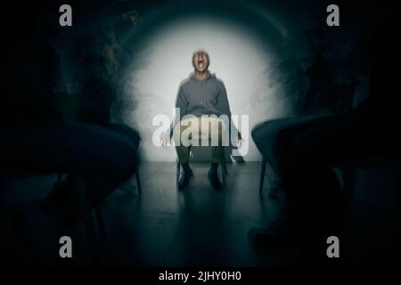 One African American male suffering mental illness in asylum. Black schizophrenic man experiencing a breakdown while being surrounded by people on a Stock Photo