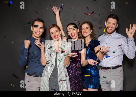 happy friends at party under confetti over black Stock Photo