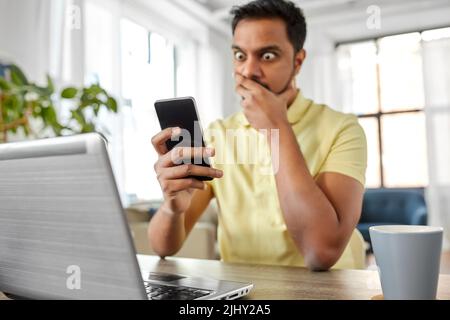 shocked indian man with smartphone working at home Stock Photo