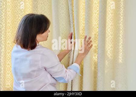 Woman touches curtains, lays out the folds on light velvet curtain Stock Photo