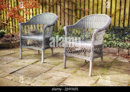 Armchairs in a relaxing garden space in a backyard of a home. Decorative outdoor furniture or woven chairs near ornamental plants. Gardening decor Stock Photo