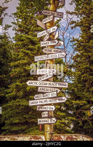July 2 2022 Denali AK USA Signpost in Healy Alaska with distances to Magic Bus Nome Seward Sarah Palins House Anchorage and more- Evergreen trees in b Stock Photo