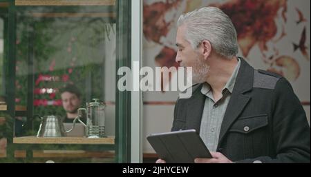Confident entrepreneur holding tablet in front of cafe store. Portrait of a happy coffee shop owner looking at results smiling feeling confidence. Sma Stock Photo