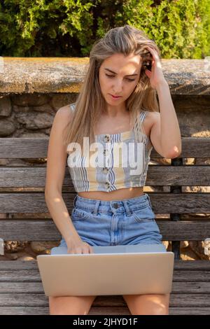 Vertical view of young woman stressed out working on her online job while enjoying the time in the park sitting on a bench Stock Photo