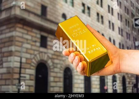 gold ingot in hand on background Federal Reserve Bank of New York. The building hosts a vault containing the world's largest depository of gold. outsi Stock Photo