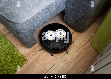 Automatic robot vacuum cleaner in black on a wooden floor . New modern technologies for apartment cleaning. smart home electronic assistant. robot vac Stock Photo