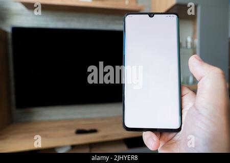 man hand tap on white screen smartphone with screen tv on background in the morning. Blank screen white screen. The form for information. Stock Photo