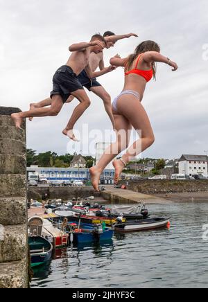 Schull, West Cork, Ireland. 21st July, 2022. On a warm and humid day with temperatures in Schull at 20C, Thomas Creagh, Trim and Noah O'Callaghan and Eve McDonald from Cork jump into the water off Schull Pier to cool down. Credit: AG News/Alamy Live News Stock Photo