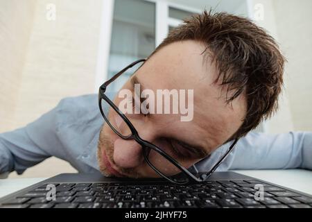 Close-up image of tired Sleepy businessman sleeping on his laptop against the white surface. A tired programmer in the office. A hungover morning at w Stock Photo