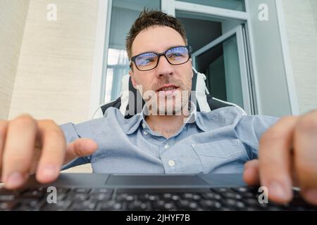 A young handsome man in a blue shirt is working at a computer on a light background. The programmer is focused on work. Stock Photo