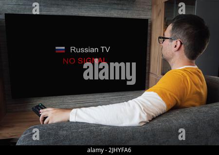 The concept of disconnecting Russian channels in Europe and the USA. Blocking of Russian TV broadcasting. Young handsome man watching TV on a sofa at Stock Photo