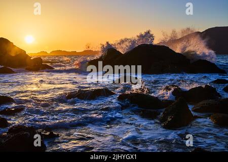 Waves crashing over boulders on ocean during sunset Stock Photo
