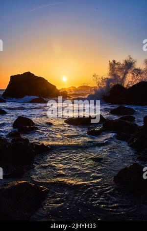 Waves crashing over rocks during beautiful sunset in California Stock Photo