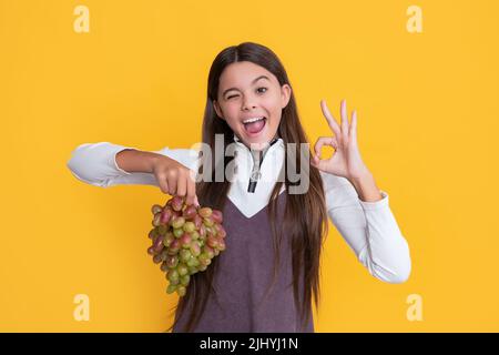 positive child holding fresh grapes fruit on yellow background Stock Photo