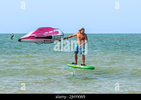 Wing foiling / wing surfing on the North Sea showing wingboarder / wing boarder standing on foilboard / hydrofoil board and holding an inflatable wing Stock Photo