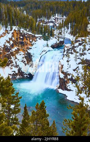 Winter at Yellowstone with snowy cliffs by Lower Falls surrounded in pine trees Stock Photo