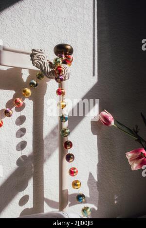 festive boho bed decor with colorful ball garland on vintage white metal bed frame in the sunlight, bed party Stock Photo