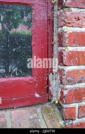 Closeup of abandoned red window covered in spiderwebs from neglect, poverty and economic crisis. Empty, old and dirty residential brick building or Stock Photo