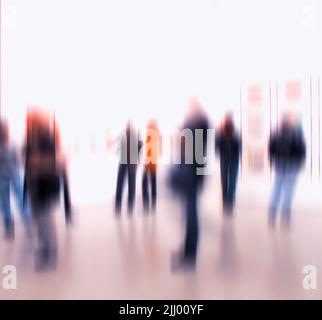 Blurred people browsing and looking at display at an art exhibition or museum. Group of businesspeople networking at a trade fair. Big room or hall Stock Photo