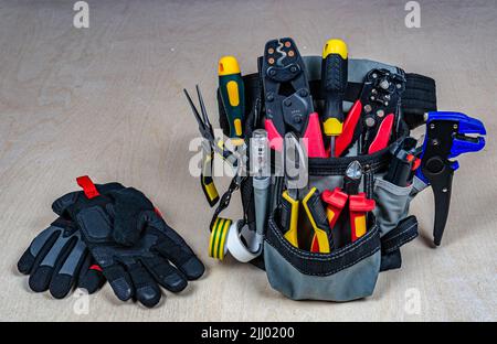 Electrician's bag with a professional electric tools and gloves. Pliers, wire cutters, strippers, screwdrivers, testers, crimping pliers. Plywood back Stock Photo