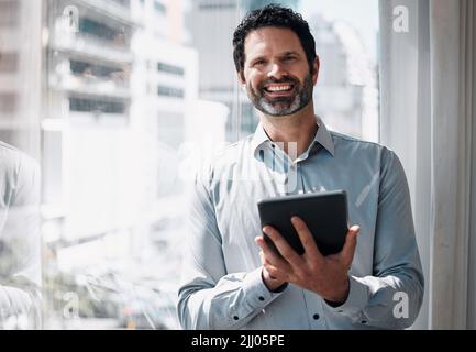 I manage my teams schedule. a mature businessman standing alone in the office and using a digital tablet. Stock Photo