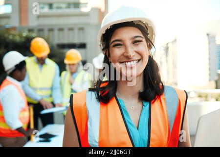 Building is my passion. an attractive young contractor standing outside while her colleagues work behind her. Stock Photo