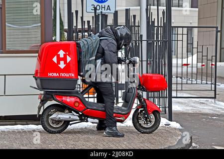 unknown young Nova Poshta courier in black suit on motorcycle delivers items in large red container. Stock Photo
