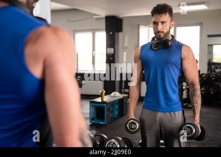 Handsome male with tattoos in his 20s training in the gym with mirror Stock Photo