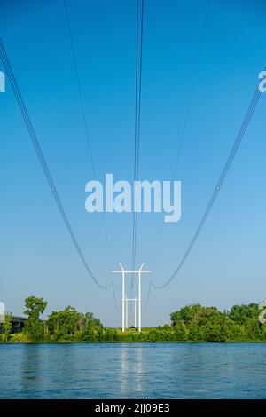 Columns of modern electric power distribution poles with cables crossing a river in a rural region. Stock Photo