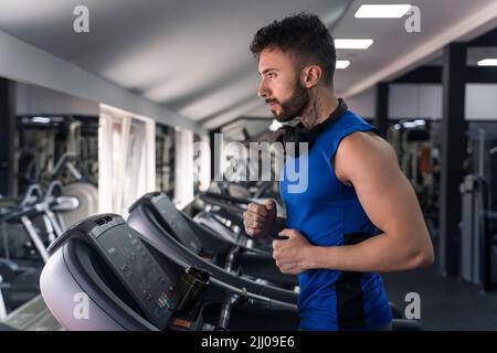 Handsome male with tattoos in his 20s running on the treadmill in the gym Stock Photo
