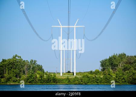 Columns of modern electric power distribution poles with cables crossing a river in a rural region. Stock Photo