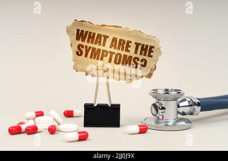 Medical concept. Near the stethoscope are pills and a clip with a cardboard sign - What are the symptoms Stock Photo