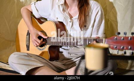 Young Asian female musician playing guitar and singing with her friends during having a bonfire party at night in the campground. cropped image Stock Photo