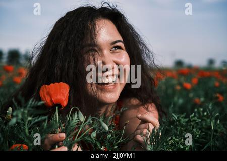 Asian girl in a red dress lays in a poppy field, happy Stock Photo