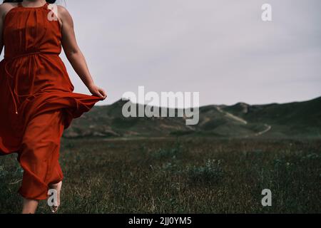 A girl in a red dress running on the field, mountains. Stock Photo