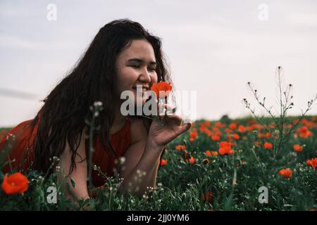 Asian girl in a red dress sits in a poppy field, happy Stock Photo