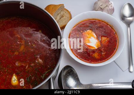 Ukrainian borscht, red soup in saucepan and in white bowl with sour cream, garlic, pepper, homebaked bread. Food and health. selective focus Stock Photo