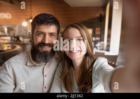 Smiling beautiful woman and her handsome boyfriend. Couple at their date in restaurant. Happy cheerful family. They taking Pov selfie at cafe Stock Photo